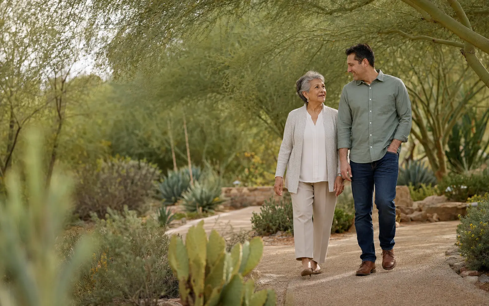 A senior woman and her adult child walking together in a shaded Arizona garden